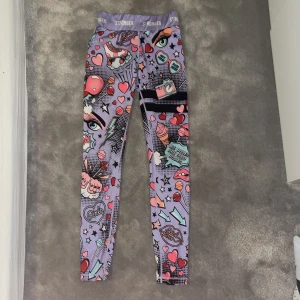 Träningstights från Stronger - Säljer ett par färgglada leggings med hög midja från Stronger med ett unikt mönster av ögon, hjärtan och cupcakes💗💗 De har en tight passform och är perfekta för träning eller en färgglad vardagslook🌟Lite noppriga!