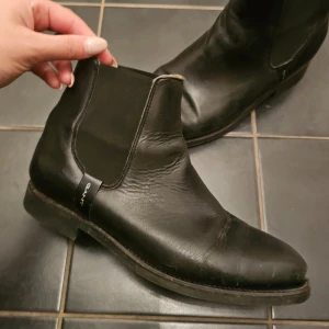 Svarta Chelsea boots från Gant - Snygga svarta Chelsea boots från Gant i skinn. De har en klassisk design med elastiska paneler på sidorna för enkel på- och avtagning. Perfekta för en stilren look.