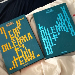 DIMENSION : DILEMMA - Två exemplar av albumet 'DIMENSION : DILEMMA' av ENHYPEN. Omslagen har en modern design med text i gult och turkost på en mörk bakgrund. Perfekt för fans av K-pop och samlare av musikalbum. Båda-300kr En-150kr