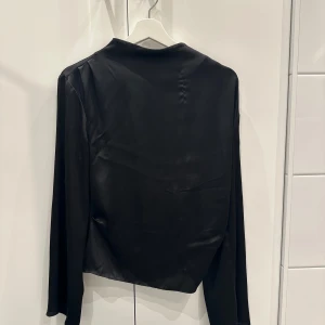 Svart långärmad topp - Elegant svart långärmad topp i ett mjukt och glansigt material. Perfekt för en stilren look. På bilden ser man ett märke av en tråd men dock inget som syns tydligt när den sitter på💕 bara att höra av sig för fler bilder på, 