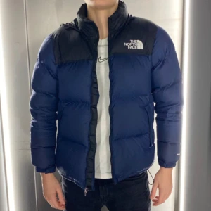 Mörkblå puffar från The North Face - Säljer en snygg blå dunjacka från The North Face med svarta axelpartier. Jackan har en dragkedja framtill och är långärmad. Perfekt för kyliga dagar.