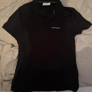 Svart pikétröja från Calvin Klein Jeans - Snygg svart pikétröja från Calvin Klein Jeans med klassisk krage och korta ärmar. Perfekt för en stilren look. Diskret logga på bröstet.