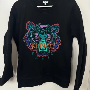 Kenzo tröja strl M - Snygg svart tröja från Kenzo med ett färgglatt tigerbroderi på framsidan. Tröjan har långa ärmar och en rund halsringning. Perfekt för att ge din outfit en cool touch.
