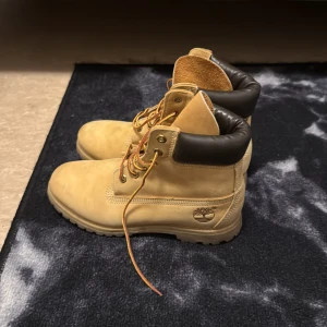 Beige boots från Timberland - Säljer ett par klassiska beige boots från Timberland med snörning och vadderad krage. Perfekta för höst och vinter med sin robusta design och slitstarka material.