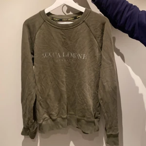Olivgrön tröja från Acqua Limone - Snygg olivgrön tröja från Acqua Limone med ett gult citronmönster på baksidan. Tröjan har långa ärmar och rund halsringning. Perfekt för en avslappnad stil.