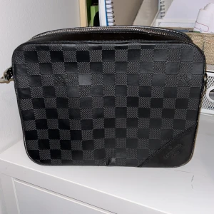 Svart rutig axelväska - Snygg svart axelväska med ett klassiskt rutigt mönster. Väskan har en dragkedja upptill och är perfekt för att bära dina dagliga nödvändigheter. Den stilrena designen gör den lätt att matcha med olika outfits.