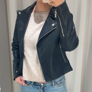 Svart skinnjacka med dragkedja - Snygg svart skinnjacka med asymmetrisk dragkedja och silverfärgade detaljer. Jackan har en klassisk bikerstil med långa ärmar och dragkedjor vid ärmsluten. Har kostat 400kr säljer de för halva priset🩷