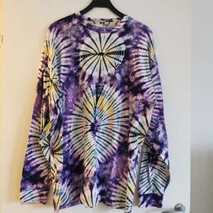 Flerfärgad tie-dye tröja från Vans - Säljer en cool flerfärgad tie-dye tröja från Vans i storlek XL. Tröjan har ett unikt mönster i lila, gul och svart med långärmade ärmar. Perfekt för en avslappnad stil!