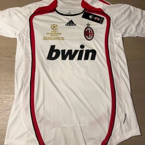 Vit AC Milan fotbollströja med Kaka 22 - Säljer en vit AC Milan fotbollströja från Adidas med Kaka och nummer 22 på ryggen. Tröjan har röda och svarta detaljer samt korta ärmar. Perfekt för fans av laget och spelaren!