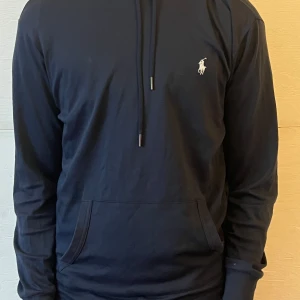   Ralph Lauren hoodie - Säljer en stilren mörkblå hoodie från Ralph Lauren med det klassiska logotypen på bröstet. Tröjan har en justerbar huva med snören och en praktisk magficka. Perfekt för en avslappnad look. 🧢
