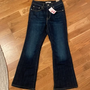 Mörkblå bootcut jeans från Levi's - Snygga mörkblå bootcut jeans från Levi's med klassisk femficksdesign och kontrastsömmar. Perfekta för en avslappnad stil med en touch av retro. Märkeslappen syns tydligt på baksidan.