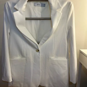 Vit kavaj från Bershka - Snygg vit kavaj från Bershka i klassisk design. Kavajen har en enkel knapp framtill och två fickor. Perfekt för en stilren look. Har axel vaddering och slits baktill. 