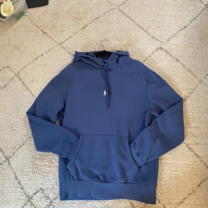 Blå hoodie från Polo Ralph Lauren - RL hoodie i väldigt bra skick. Har bara använt denna tröja 4 gånger. En liten fläck på magen som knappas syns och den går säkert bort i tvätten