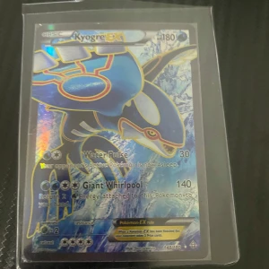 Kyogre EX Pokémonkort - Säljer ett Kyogre EX Pokémonkort med holografisk yta. Kortet har attacker som Water Pulse och Giant Whirlpool. Perfekt för samlare eller spelare som vill förstärka sin kortlek med en kraftfull vatten-Pokémon.