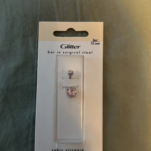 Piercingsmycke med rosa cubic zirconia - Piercingsmycke från Glitter med en rosa cubic zirconia-sten. Tillverkat i kirurgiskt stål med en stavlängd på 10 mm. Perfekt för att ge en glittrig touch till din stil.