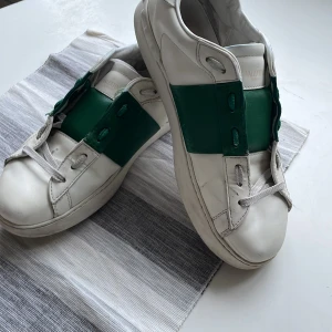 Grön vita Valentino open - Snygga vita sneakers från Valentino med gröna detaljer. Skick 6/10 Baksidan av sulan har sjunkit ner lite och det finns ett litet hål längst bak på sulan, men bortsett från de så är det bara att tvätta dom lite. Priset är inte hugget i sten.