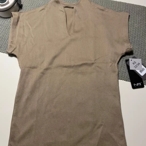 Beige ribbad topp  - Säljer en stilren beige ribbad träningstopp Toppen har en v-ringad design och korta ärmar, perfekt för en avslappnad look. 