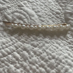 Hårspänne med pärlor - Elegant hårspänne dekorerat med vita pärlor på en guldig bas. Perfekt för att ge en stilfull touch till din frisyr.