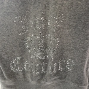 Grå hoodie från Juicy Couture - Säljer min gråa zip hoodie från Juicy Couture med glittrande stenar som bildar logotypen och en krona på ryggen. Jätte bra skick, Storlek L men passar även M och S då den är lite mindre i storlek. SÄLJS INTE BILLIGARE