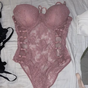 Rosa spetsbikini med snörning - Snygg rosa spetsbikini med vadderade kupor och snörning på sidorna. Den har en elegant design med spetsdetaljer och en öppen rygg. Perfekt för en dag på stranden eller vid poolen.