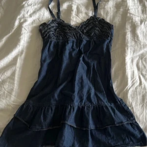 Mörkblå klänning med spetsdetaljer - Charmig mörkblå klänning med spetsdetaljer på bysten och volang i nederkant. Man kan ha klänningen antigen axelbandslös eller med axelband. Perfekt för sommarens varma dagar. 