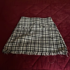 Rutig kjol från C&A - Snygg rutig kjol från C&A i svart och vit med fransiga detaljer vid fållen. Kjolen har en klassisk A-linjeform och är perfekt för en stilren look. Den är tillverkad i ett mjukt och bekvämt material som ger en skön passform. På framsidan finns även 2 fejkfickor som en fin detalj!