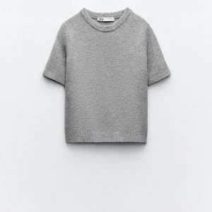 Grå stickad tröja från Zara - Säljer en stilren grå stickad tröja från Zara. Tröjan har korta ärmar och en rund halsringning, perfekt för lager på lager-stil. Den är mjuk och bekväm, idealisk för både vardag och avslappnade tillfällen.