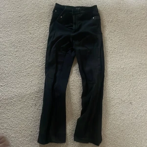 Svarta jeans med bootcut - Snygga svarta jeans med bootcut-stil och hög midja. Perfekta för en stilren look. Byxorna har en klassisk design med knappar och dragkedja framtill.