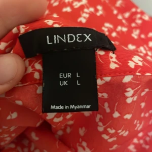 Röd blommig klänning från Lindex - Säljer en röd klänning från Lindex med ett sött blommönster i vitt. Klänningen har en knytning i midjan och är perfekt för sommarens varma dagar. Den är tillverkad i ett lätt och luftigt material som ger en skön känsla.