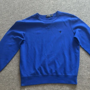 Blå tröja från Ralph Lauren - Säljer en stilren blå tröja från Ralph Lauren med det klassiska broderade logotypen på bröstet. Tröjan har långa ärmar och en rund halsringning. Perfekt för en avslappnad och snygg look. (PRIS KAN DISKUTERAS)