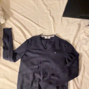 Mörkblå tröja från J.Lindeberg - Snygg mörkblå tröja från J.Lindeberg. Perfekt för en stilren look. Tröjan har långa ärmar och är tillverkad i ett mjukt material som känns skönt mot huden.