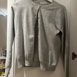 Grå kofta  - Säljer en stilren grå kofta från primark. Den har långa ärmar och knappar framtill. Perfekt för lager-på-lager under kyligare dagar.