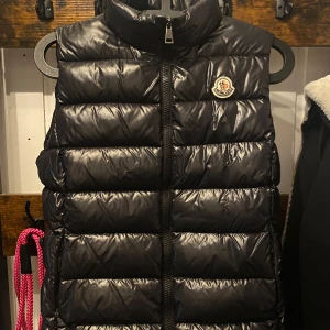Svart dunväst från Moncler - Snygg svart dunväst från Moncler med dragkedja. Perfekt för kyliga dagar när du vill hålla stilen. Västen har Monclers logga på bröstet. Västen är äkta som allt annat i min profil. Använd Max 10 gånger