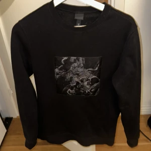 Svart tröja med konstmotiv - Snygg svart tröja med ett unikt konstmotiv på framsidan. Tröjan har långa ärmar och en rund halsringning, perfekt för en stilren look.