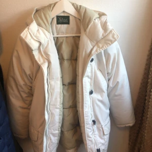 Vit dunjacka från Peak Performance - Säljer en vit dunjacka från Peak Performance med dragkedja och knappar. Jackan har en justerbar huva och praktiska fickor framtill. Perfekt för kalla vinterdagar. Pris kan förhandlas!