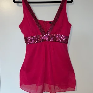 Rosa paljettlinne från Jennifer Taylor - Snygg rosa topp från Jennifer Taylor med glittrande paljettdetaljer längs axelbanden och midjan. Toppen har en dragkedja i ryggen och är perfekt för festliga tillfällen! Säljer då den tyvärr inte kommer till användning