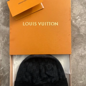  Louis Vuitton mössa - Elegant svart mössa från Louis Vuitton med diskret rutigt mönster. Mössan har en broderad logotyp framtill och är tillverkad i ett mjukt material som passar perfekt för kyligare dagar. Låda och kvitto medföljer.
