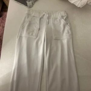 Vita mjukisbyxor från Juicy Couture - Säljer ett par vita mjukisbyxor från Juicy Couture i storlek XS. Byxorna har snörning i midjan och praktiska fickor både fram och bak. Perfekta för en avslappnad stil.