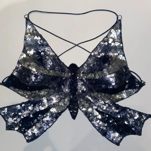 Svart paljettprydd topp - Snygg svart och silvrig topp med paljetter i fjärilsform. Tunna axelband som korsas och knyts i ryggen. Perfekt till en fest  eller nyår ✨Jag skulle säga att storleken är S/M. 