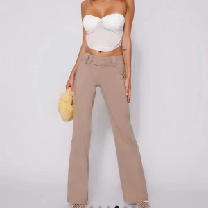 Beige byxor med låg midja - Snygga beige byxor med låg midja och bootcut-stil. Byxorna har dekorativa knappar framtill och fickor bak. Köpta från tigermist, jättenya har aldrig använt. Betalade ungefär 900 kr för de, tullen kostade också ungefär 300 kr. Passar super för mig som brukar ha 38 i jeans, dom är stretchiga