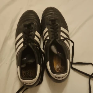 Svarta fotbollsskor från Adidas - Säljer ett par klassiska svarta Adidas Copa Mundial fotbollsskor med vita detaljer och snörning. Skorna har dobbar för bra grepp på planen och är perfekta för fotbollsträning och matcher. De är i bra skick bara lite smutsiga
