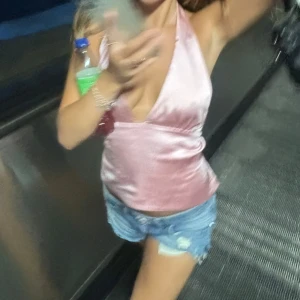 Rosa satinlinne - Snygg rosa satinlinne med djup v-ringning och halterneck-design. Perfekt för en utekväll eller fest. Linnet har en glansig finish som ger en lyxig känsla. Öppen rygg