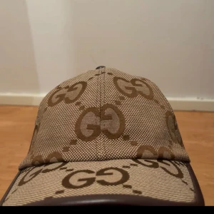 Beige Gucci jumbo  - Snygg beige keps från Gucci med det ikoniska GG-mönstret i beige. Kepsen har en klassisk design med rundad skärm och justerbar rem baktill för perfekt passform. Perfekt för att ge din outfit en lyxig touch. Priset kan diskuteras vid snabb affär. Byten går ochså