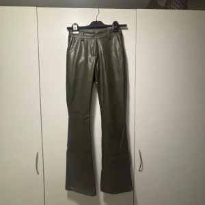Olivgröna skinnbyxor från Design by Si - Snygga olivgröna skinnbyxor med bootcut-stil från Design by Si. Byxorna har en hög midja och stängs med dragkedja och knapp. Perfekta för att ge en trendig touch till din outfit.