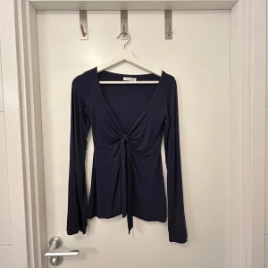 Mörkblå topp från Design by Si - Snygg mörkblå topp från Design by Si med lång ärm och knytning framtill som man kan ta bort. Öppen vid magen med utsvängda armar i storlek Medium. Endast använt en gång!                                    Perfekt middags eller fest topp!🤩
