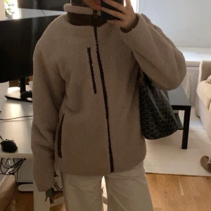 Beige teddyjacka  - Mysig beige teddyjacka med dragkedja och hög krage. Perfekt för kyliga dagar med sin fluffiga textur och bekväma passform. Jackan har praktiska fickor och en stilren design.