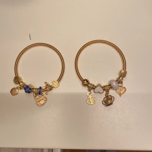 Guldarmband med berlocker - Två stiliga guldarmband med olika berlocker. Det ena armbandet har en blå blomma, en nalle och en 'I love you'-berlock. Det andra armbandet har ett ankare, ett hjärta och en krona. Perfekta för att ge en personlig touch till din stil. Säljer det 50 kr styck☺️