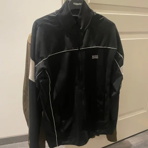 Boss kofta - Snygg svart tröja med krage från Boss med dragkedja och vita detaljer. 