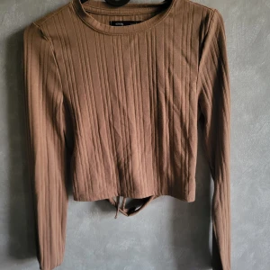 Beige/Brun ribbad topp från Sinsay - Snygg begie/brun ribbad topp från Sinsay med långärmad design och en öppen rygg med knytning. Perfekt för en trendig look.