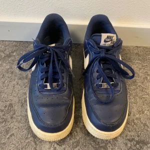 Blå Nike Air Force 1 sneakers - Snygga blå Nike Air Force sneakers med vit sula och klassisk snörning. Perfekta för en sportig look med den ikoniska Nike-loggan på sidan.                         Låda saknas 